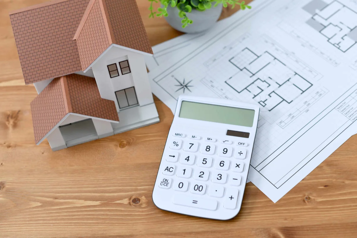 A calculator and a model house resting on a set of floor plans.