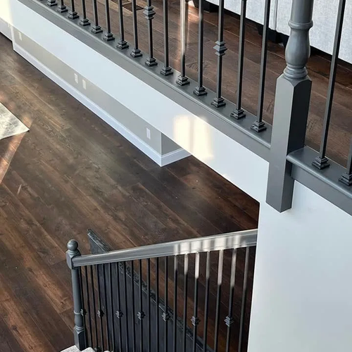 Dark plank flooring on an upstairs landing beside a black iron stair railing.