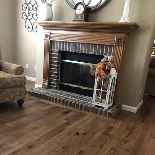Warm brown wood plank flooring in a living room in front of a brick fireplace.