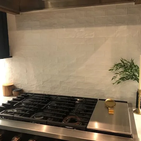 White handmade look wall tile set behind a stainless gas cooktop.