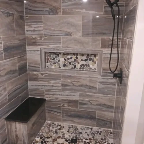 Tiled shower with marbled wall tile, a pebble floor and a recessed accent niche.