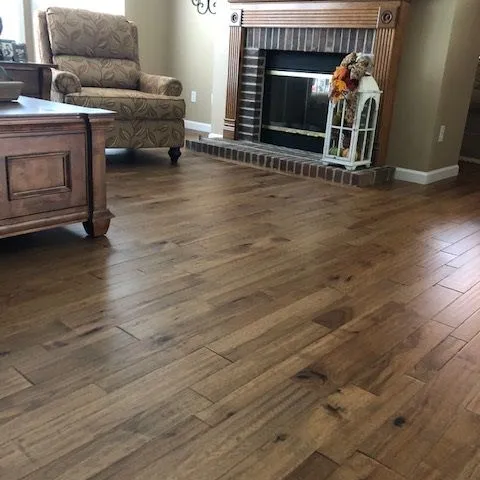 Medium brown wood plank flooring across a living room with a fireplace and a recliner.