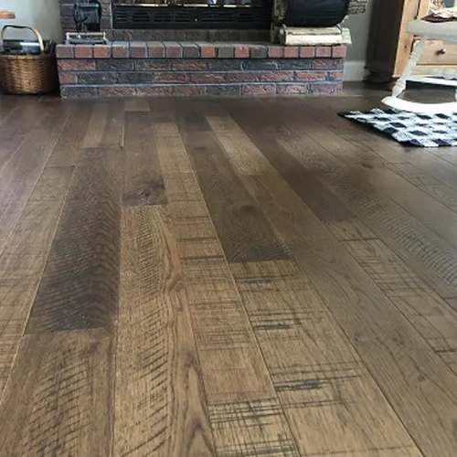 Hand scraped wide plank wood flooring beside the brick base of a fireplace.