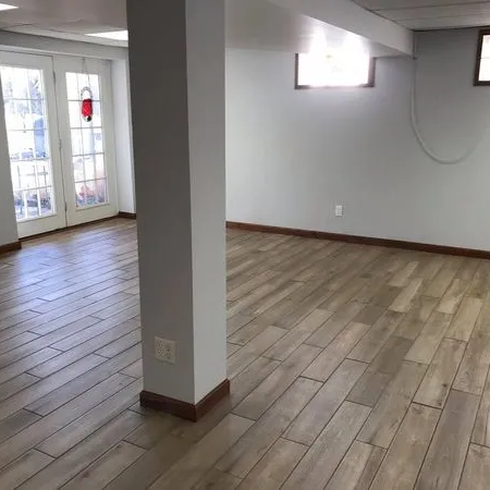 Grey wood look tile plank across a finished basement with French doors.